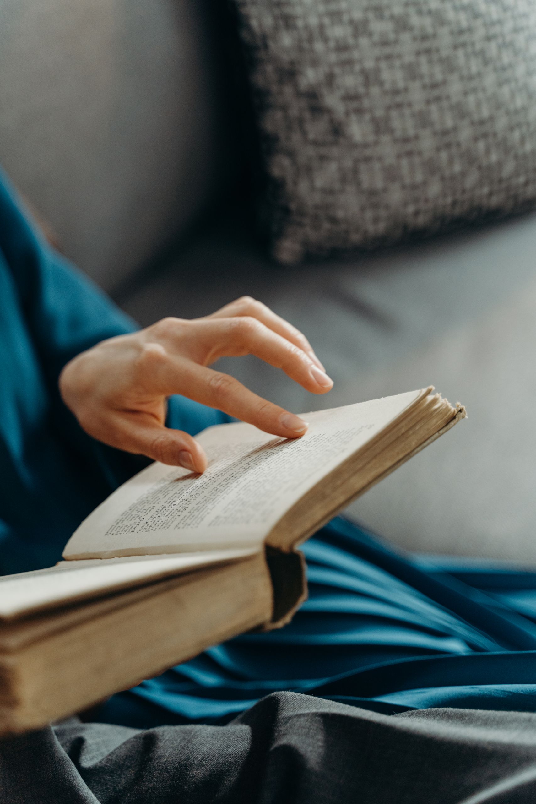 A close-up view of a person's hand turning a page in a book while seated indoors.