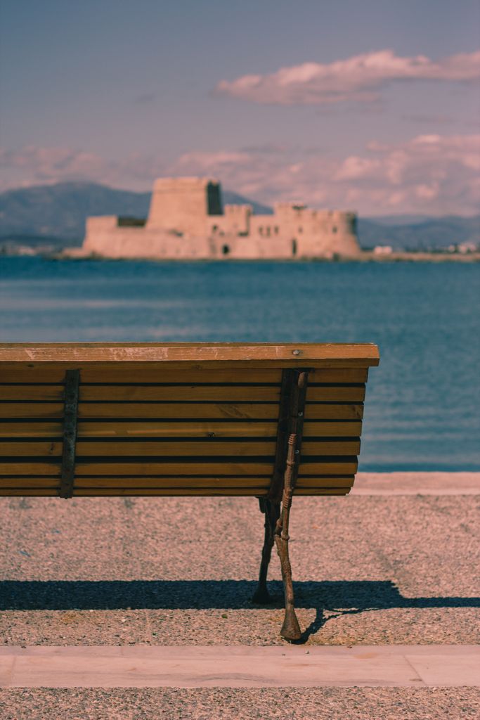 A peaceful seaside scene with a bench overlooking a historic castle across the water.
