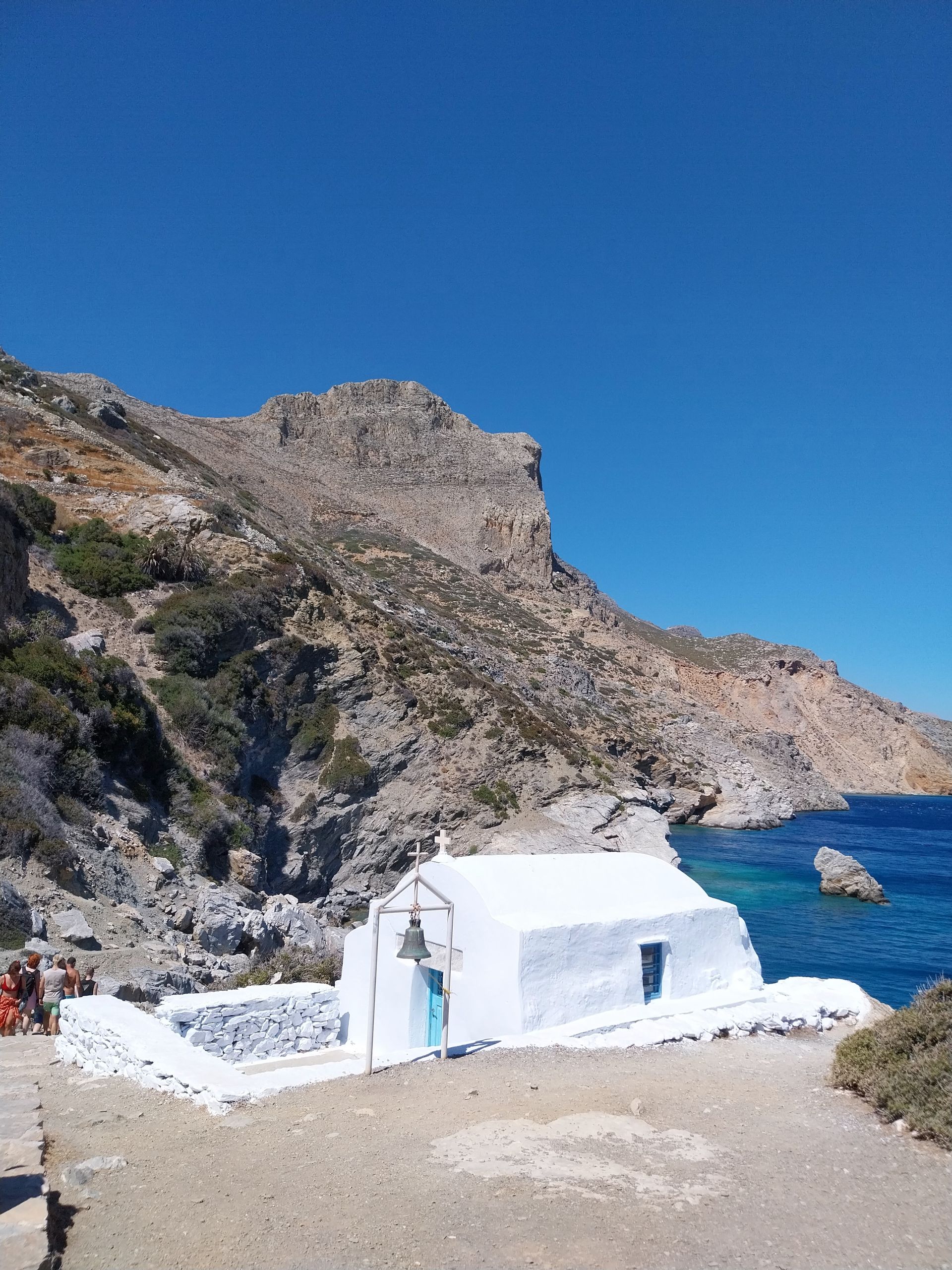Scenic view of a whitewashed chapel nestled by the rocky coastline of Amorgos, Greece.